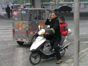 Elektroskůtry v Pekingu jsou běžné, ty se spalovacím motorem jsou raritou. S předpisy si ale hlavu nelámou, jízda bez helmy nebo na červenou jsou běžné. V pozadí je elektro-drožka.